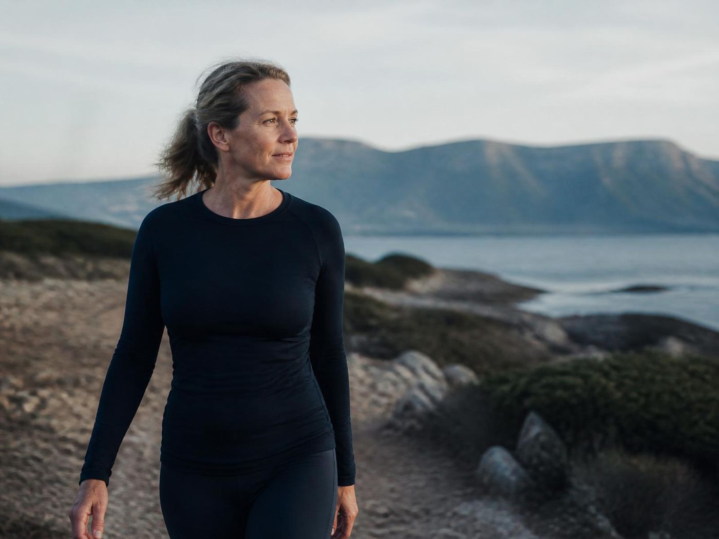 A woman in her early 50s walking confidently outdoors in soft morning light.