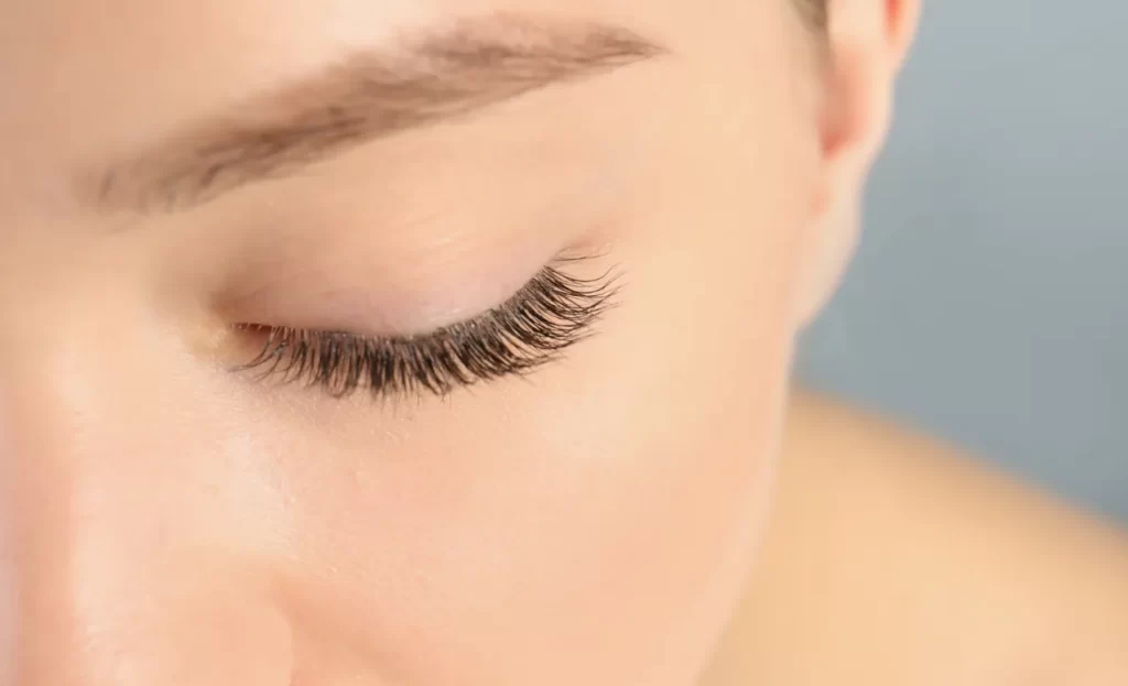 young woman with beautiful long eyelashes on gray utc